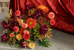 Bouquet of burgundy dahlias and marigolds resting against a bed of deep red velvet