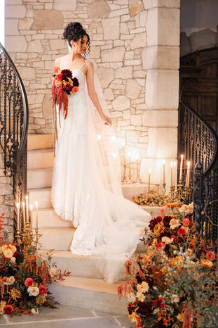Bride descending a candlelit stone staircase, wine-toned bouquet in hand