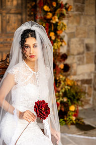 Bride in a cathedral veil holding a bold red dahlia bouquet before a stone tower