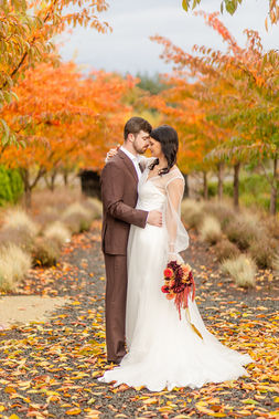 Bride and groom embracing on a path carpeted with fallen autumn leaves