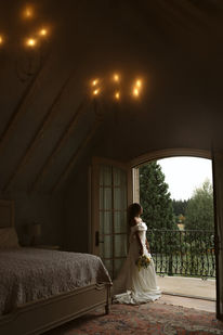 Bride in a rustic attic bedroom looking toward an open balcony door