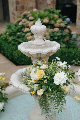 Stone garden fountain topped with a lush white and yellow floral arrangement