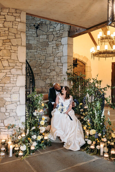 Bride and groom sharing a tender moment on candlelit stone steps lined with flowers