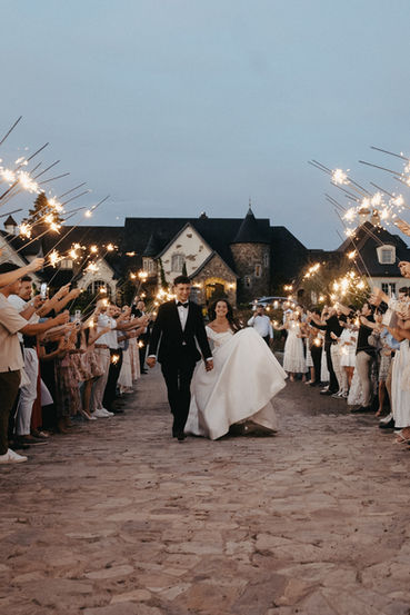 Guests waving sparklers as the newlyweds walk the cobblestone path at dusk